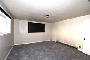 Spare room featuring baseboard heating, dark colored carpet, and a textured ceiling