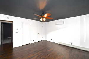 Unfurnished bedroom featuring a baseboard heating unit, multiple closets, dark wood-style flooring, a wall mounted AC, and a ceiling fan