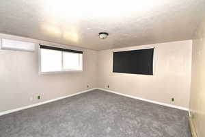 Spare room featuring a textured ceiling, carpet flooring, a wall mounted air conditioner, and baseboard heating