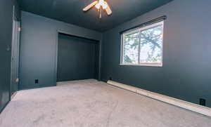 Unfurnished bedroom featuring a baseboard radiator, carpet floors, a ceiling fan, and a closet