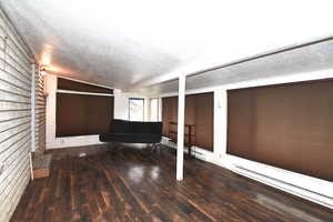 Interior space with baseboard heating, a textured ceiling, lofted ceiling, dark wood-type flooring, and brick wall