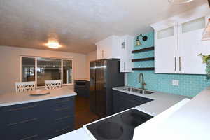 Kitchen featuring white cabinetry, tasteful backsplash, a textured ceiling, glass insert cabinets, and dark wood-style floors