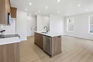 Kitchen featuring stainless steel appliances, recessed lighting, light wood-style floors, a kitchen island with sink, and brown cabinets