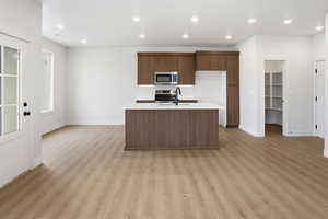 Kitchen featuring stainless steel appliances, a center island with sink, recessed lighting, light wood-type flooring, and brown cabinetry