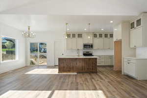 Kitchen featuring a center island with sink, hanging light fixtures, recessed lighting, glass insert cabinets, and appliances with stainless steel finishes