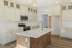 Kitchen featuring glass insert cabinets, appliances with stainless steel finishes, an island with sink, wood finished floors, and recessed lighting