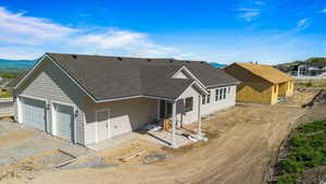 View of front of property with roof with shingles, dirt driveway, a garage, and a patio