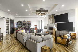 Living room featuring a raised ceiling, recessed lighting, a barn door, wood-type flooring, and a glass covered fireplace