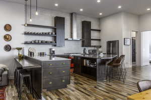 Bar area with open shelves, wall chimney exhaust hood, high quality appliances, dark brown cabinets, and pendant lighting