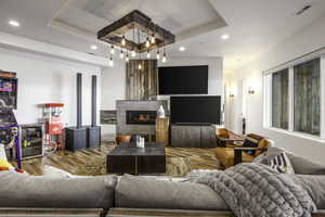 Living room with a tray ceiling, recessed lighting, wood finished floors, a glass covered fireplace, and beverage cooler