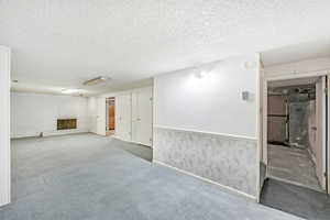 Finished below grade area with a textured ceiling, carpet, brick wall, and wainscoting
