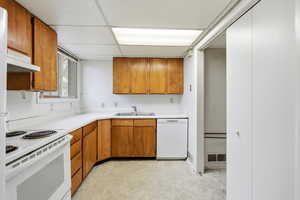 Kitchen with white appliances, brown cabinets, light countertops, a paneled ceiling, and under cabinet range hood