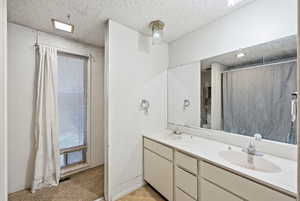 Bathroom featuring curtained shower, double vanity, and a textured ceiling