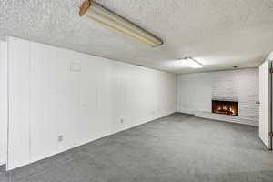 Below grade area featuring a brick fireplace, carpet flooring, wooden walls, a textured ceiling, and brick wall