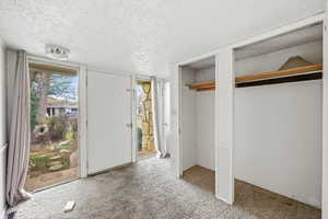Unfurnished bedroom featuring a textured ceiling, carpet, two closets, and access to outside