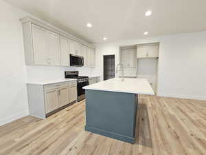 Kitchen with gray cabinetry, stainless steel appliances, recessed lighting, and a kitchen island with sink