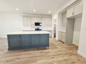 Kitchen with gray cabinetry, an island with sink, stainless steel range, recessed lighting, and light wood-style flooring