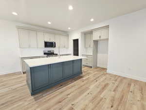 Kitchen with recessed lighting, gray cabinetry, appliances with stainless steel finishes, a center island with sink, and light wood finished floors