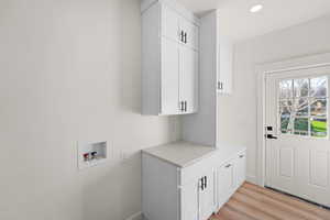 Laundry room with hookup for a washing machine, cabinet space, and light wood finished floors