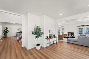 Living room with french doors, light wood-type flooring, a glass covered fireplace, recessed lighting, and stairs