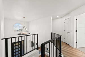 Hallway featuring an upstairs landing, light wood-style flooring, a chandelier, and recessed lighting