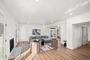 Living room with light wood-style floors, a glass covered fireplace, recessed lighting, and french doors