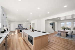 Kitchen featuring open floor plan, light wood-style floors, light stone countertops, a kitchen bar, and recessed lighting
