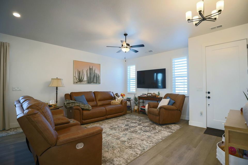 Living area featuring dark wood-style flooring, a ceiling fan, and a chandelier
