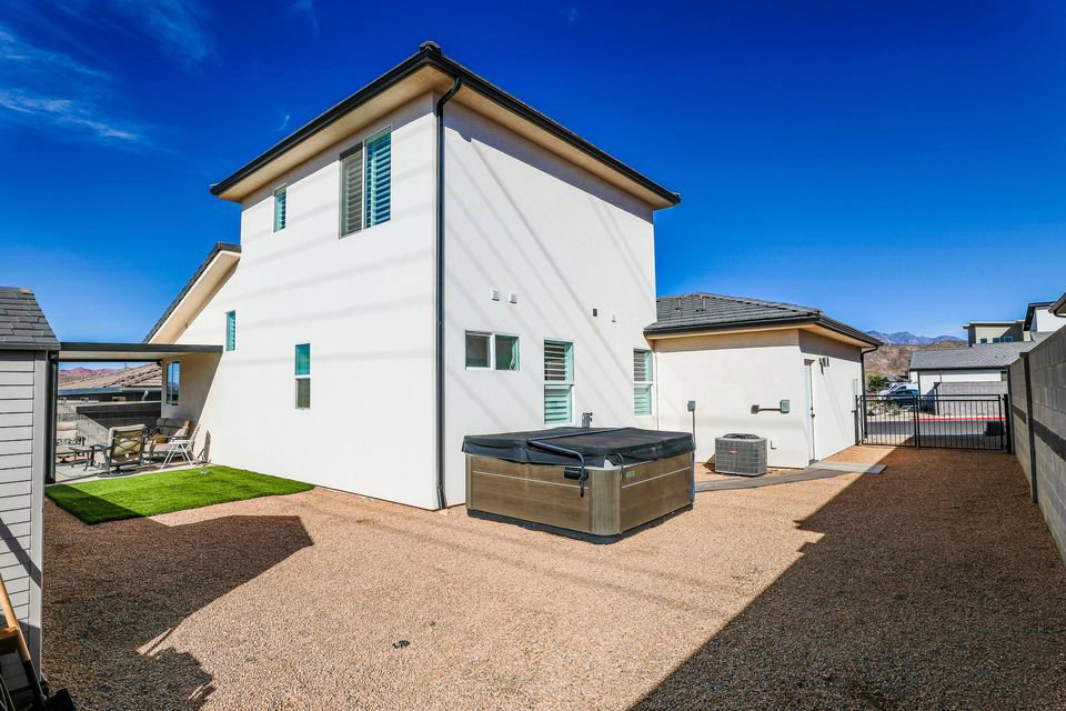 Rear view of property featuring a hot tub, stucco siding, a patio, and a gate