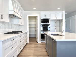 Kitchen featuring white cabinetry, premium range hood, light wood-type flooring, light stone counters, and recessed lighting