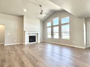 Unfurnished living room with light wood-type flooring, ceiling fan, a stone fireplace, and high vaulted ceiling