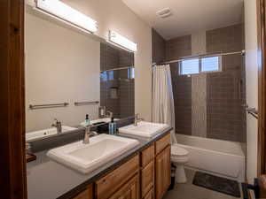 Secondary Bathroom featuring double vanity, shower / bath combo with shower curtain, and dark tile patterned flooring