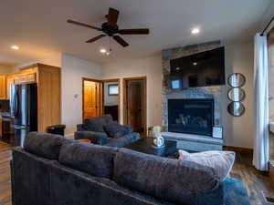 Living room with dark wood-style flooring, a stone fireplace, ceiling fan, and recessed lighting