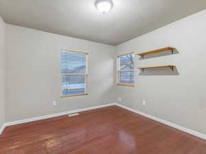 Empty room featuring dark wood-type flooring and a textured ceiling