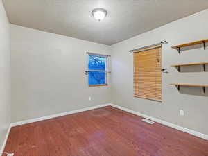 Empty room with a textured ceiling and dark wood-style flooring