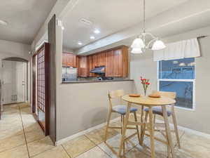 Kitchen featuring brown cabinets, stainless steel fridge with ice dispenser, hanging light fixtures, a chandelier, and light tile patterned flooring