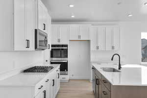 Kitchen with light stone counters, white cabinetry, appliances with stainless steel finishes, recessed lighting, and light wood-style flooring