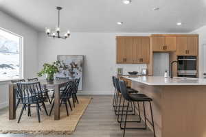Kitchen featuring light wood finished floors, a chandelier, light stone counters, a breakfast bar area, and a kitchen island with sink