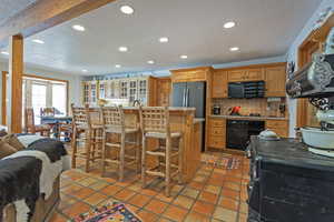 Kitchen featuring a kitchen bar, a textured ceiling, black appliances, an island with sink, and recessed lighting
