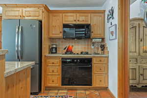 Kitchen with black appliances, backsplash, light tile patterned floors, a textured ceiling, and light stone countertops