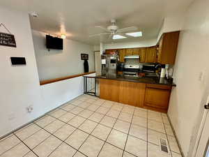 Kitchen with brown cabinetry, stainless steel appliances, ceiling fan, a peninsula, and light tile patterned flooring