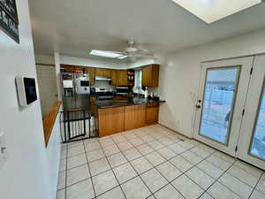 Kitchen with brown cabinetry, appliances with stainless steel finishes, a skylight, a peninsula, and a ceiling fan