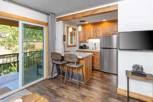 Kitchen featuring light countertops, freestanding refrigerator, a kitchen bar, decorative light fixtures, and brown cabinets