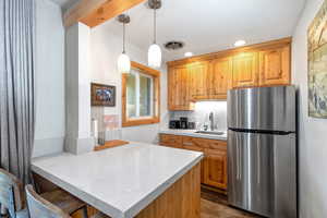 Kitchen featuring freestanding refrigerator, a kitchen bar, dark wood finished floors, pendant lighting, and a peninsula