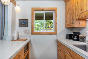 Kitchen with light stone countertops, decorative light fixtures, brown cabinetry, and backsplash