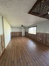 Unfurnished living room featuring wainscoting, a textured ceiling, dark wood finished floors, ceiling fan, and wood walls