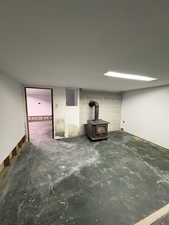 Unfurnished living room with a wood stove, concrete flooring, and concrete block wall