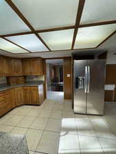 Kitchen featuring brown cabinets, stainless steel refrigerator with ice dispenser, dark countertops, and light tile patterned flooring