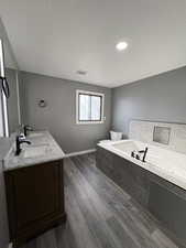 Full bathroom featuring double vanity, a textured ceiling, a whirlpool tub, dark wood-style floors, and recessed lighting
