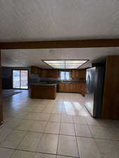 Kitchen featuring light tile patterned floors, stainless steel fridge with ice dispenser, brown cabinets, healthy amount of natural light, and a textured ceiling